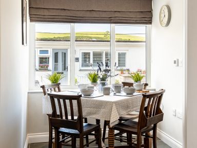 A dining area with a table set for four next to a window with plants and flowers at Mino Cottage in Port Isaac