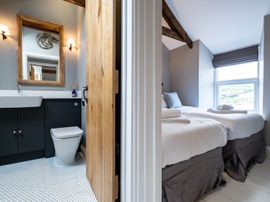 A bathroom with a mirror and toilet next to a bedroom with two beds at Mino Cottage in Port Isaac