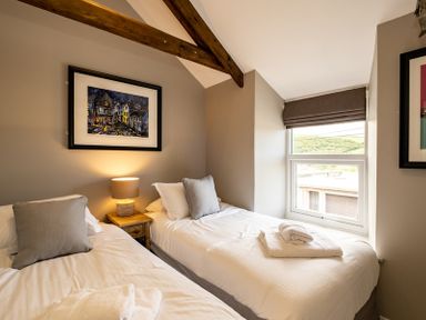 A bedroom with two single beds a wooden nightstand with a lamp and a window at Mino Cottage in Port Isaac