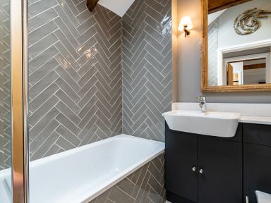 A bathroom with a bathtub a sink with black cabinet a mirror and a wall light at Mino Cottage in Port Isaac