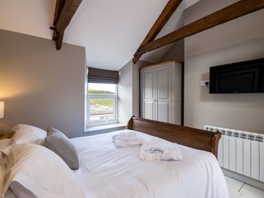A bedroom with a bed white linens wooden beams a wardrobe and a wall mounted television at Mino Cottage in Port Isaac