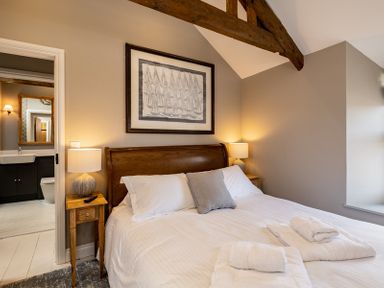 A bedroom with a wooden bedframe bedside tables with lamps folded towels on the bed and a bathroom visible through an open door at Mino Cottage in Port Isaac