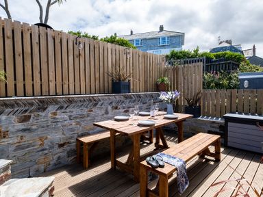 An outdoor wooden dining table with benches set with plates and glasses in a fenced patio at Mino Cottage in Port Isaac