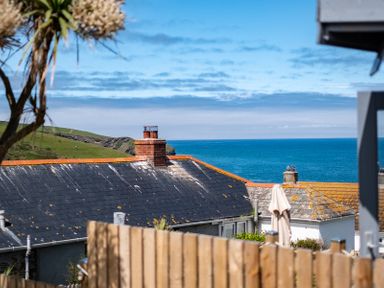 A coastal view showing rooftops with chimneys a wooden fence and the sea in the background at Mino Cottage in Port Isaac