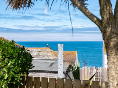 View of rooftops and sea beyond with a tree and wooden fence in the foreground at Mino Cottage in Port Isaac