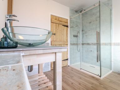 A bathroom with a glass vessel sink on a wooden vanity and a glass-enclosed shower at Bluebird Cottage in Newmarket