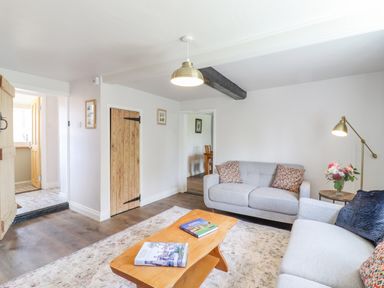 A living room with two gray sofas a wooden coffee table with books a floor lamp a side table with flowers and wooden doors at Bluebird Cottage in Newmarket