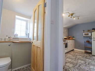 A bathroom with a toilet and sink next to a kitchen with cabinets and appliances at Bluebird Cottage in Newmarket