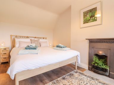 A bedroom with a bed with folded towels a bedside table and a fireplace with plants at Bluebird Cottage in Newmarket