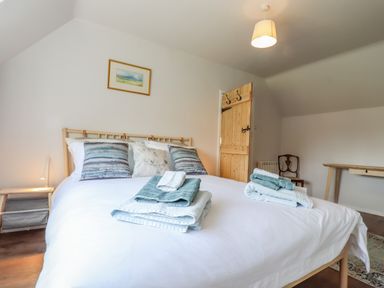 A bedroom with a bed with folded towels pillows a wooden door and desk at Bluebird Cottage in Newmarket