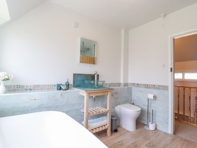 A bathroom with a bathtub, wooden sink stand with glass basin, toilet, and tiled walls at Bluebird Cottage in Newmarket