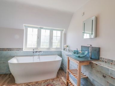 A bathroom with a white bathtub under a window and a wooden vanity with a glass sink at Bluebird Cottage in Newmarket
