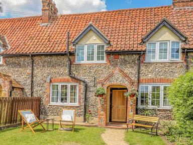 Exterior of a stone cottage with a tiled roof wooden door two chairs a small table and a bench in the garden at Bluebird Cottage in Newmarket