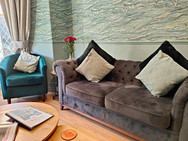 A living room with a grey sofa and teal armchair with cushions and a coffee table with magazines at Squirrel Lodge Keswick