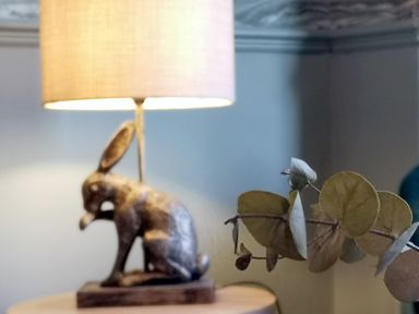 A wooden rabbit lamp on a table with a branch of dried leaves in the foreground at Squirrel Lodge in Keswick
