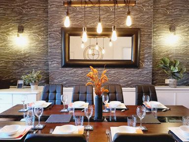 A dining room with a wooden table set for six with plates glasses and cutlery and a black vase with dried flowers in the center at Squirrel Lodge in Keswick