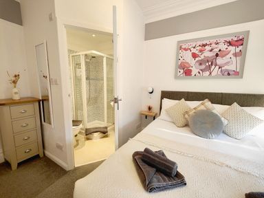 A bedroom with a double bed with cushions a bedside table and an en suite shower at Squirrel Lodge in Keswick