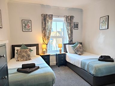 A bedroom with two single beds bedside tables lamps and framed pictures at Squirrel Lodge in Keswick