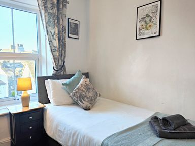 A bedroom with a single bed pillows bedside table lamp window and framed pictures at Squirrel Lodge in Keswick
