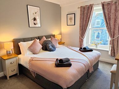 A bedroom with a double bed with pillows and folded towels by the window at Squirrel Lodge in Keswick