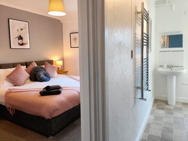 A bedroom with bed and pillows next to a bathroom with sink and towel rack at Squirrel Lodge in Keswick