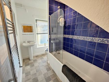 A bathroom with a bathtub and shower next to a sink and window at Squirrel Lodge in Keswick