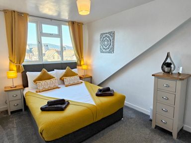 A bedroom with a double bed yellow bedding and pillows two bedside tables with lamps and a chest of drawers at Squirrel Lodge in Keswick