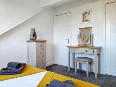 A bedroom corner with a dresser, dressing table, stool, and bed with folded towels at Squirrel Lodge in Keswick