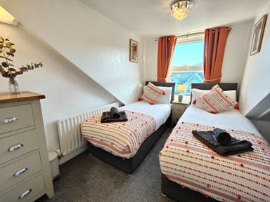 A bedroom with two single beds a window with curtains and a chest of drawers at Squirrel Lodge in Keswick
