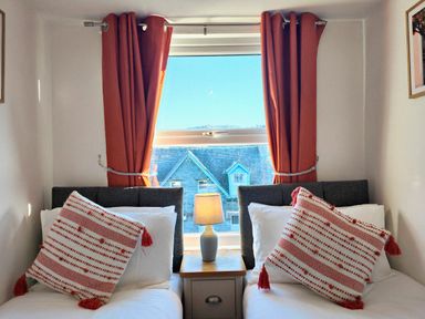 Two single beds with red and white striped pillows a lamp on a bedside table and a window with red curtains at Squirrel Lodge in Keswick