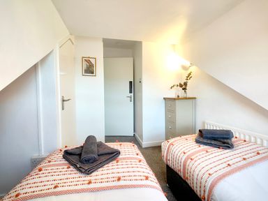 A bedroom with two single beds with folded towels a small chest of drawers and a door at Squirrel Lodge Keswick