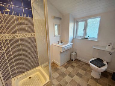 A bathroom with a shower cubicle sink with a mirror a window and a toilet at Squirrel Lodge in Keswick