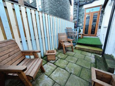 A small patio with wooden chairs wooden planters a painted wooden fence and a door leading inside at Squirrel Lodge in Keswick