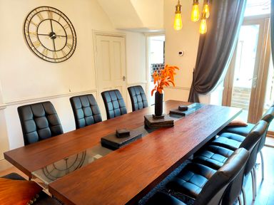 A dining room with a long wooden table black chairs a large wall clock and hanging lights at Squirrel Lodge in Keswick