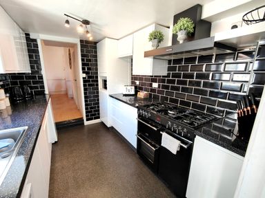 A kitchen with black tiled walls white cabinets black countertops and a black gas stove at Squirrel Lodge in Keswick