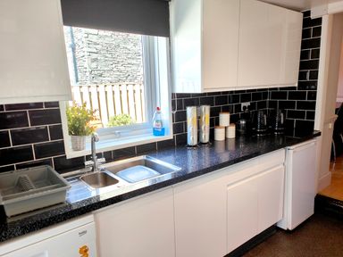 A kitchen with black tiled walls white cabinets a countertop with containers a sink and a window at Squirrel Lodge in Keswick