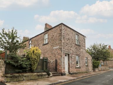 A corner view of a stone house with windows a door a black metal gate and bushes along a street at Islestone 1 Temperance Terrace in Berwick-Upon-Tweed