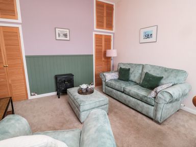 A living room with green sofas, an ottoman with a tea set, wooden closets, a small stove, and two framed pictures on the wall at Islestone 1 Temperance Terrace in Berwick-Upon-Tweed