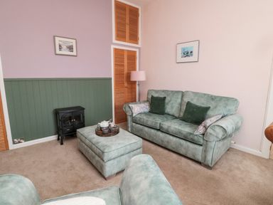 A living room with green sofas, an ottoman, a small stove, a floor lamp, and pictures on the walls at Islestone 1 Temperance Terrace in Berwick-Upon-Tweed
