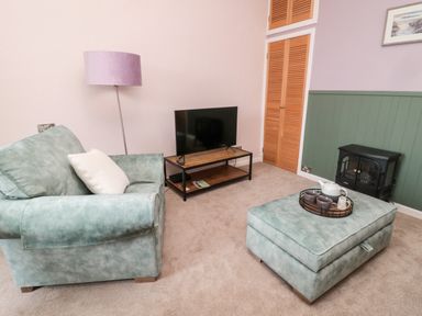 A living room with green armchair and ottoman with tea set a TV on stand and a black stove at Islestone 1 Temperance Terrace in Berwick-Upon-Tweed