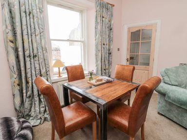 A dining area with a wooden table and four brown chairs near a window with floral curtains at Islestone 1 Temperance Terrace in Berwick-Upon-Tweed