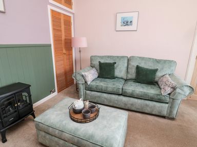A living room with a green sofa an ottoman a lamp a small stove and a painting at Islestone 1 Temperance Terrace in Berwick-Upon-Tweed
