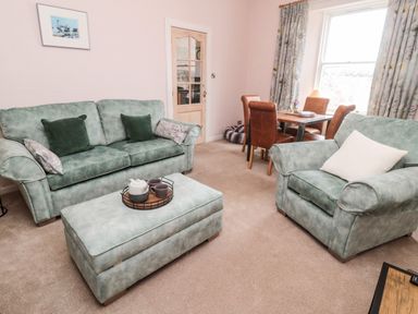 A living room with green sofas a matching ottoman and a dining table with four brown chairs at Islestone 1 Temperance Terrace Berwick-Upon-Tweed