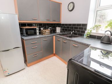 A kitchen with grey and wood cabinets a refrigerator microwave sink kettle and a clock on the wall at Islestone 1 Temperance Terrace in Berwick-Upon-Tweed