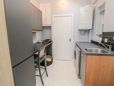 A kitchen with black cabinets a chair a washing machine a sink and a boiler at Islestone 1 Temperance Terrace in Berwick-Upon-Tweed
