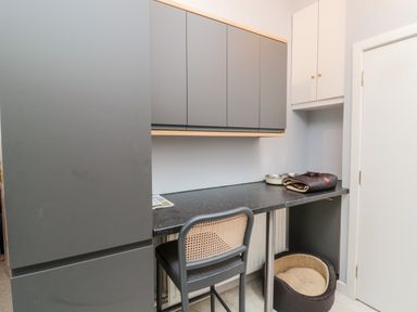 A small workspace with grey cabinets a chair a countertop with pet bowls and a pet bed under the counter at Islestone 1 Temperance Terrace Berwick-Upon-Tweed