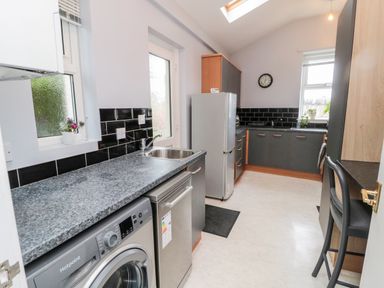A kitchen with washing machine dishwasher refrigerator black tiled backsplash and cabinets at Islestone 1 Temperance Terrace in Berwick-Upon-Tweed