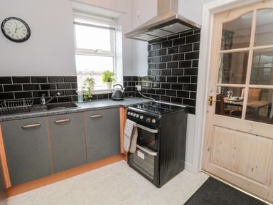 A kitchen with black tiled backsplash grey cabinets a black stove and a wooden door at Islestone 1 Temperance Terrace in Berwick-Upon-Tweed