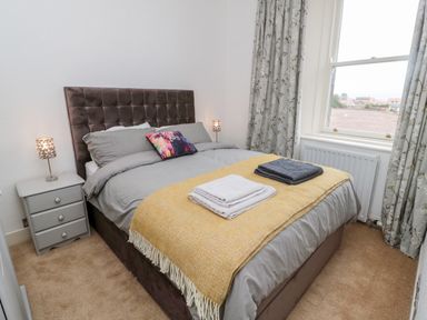 A bedroom with a bed, bedside tables with lamps, folded towels on the bed, and a window with curtains at Islestone 1 Temperance Terrace in Berwick-Upon-Tweed