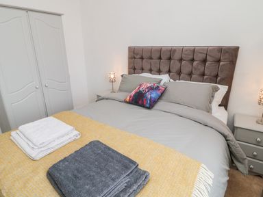 A bedroom with a bed with gray bedding and a colorful pillow two bedside tables with lamps and a gray wardrobe at Islestone 1 Temperance Terrace in Berwick-Upon-Tweed